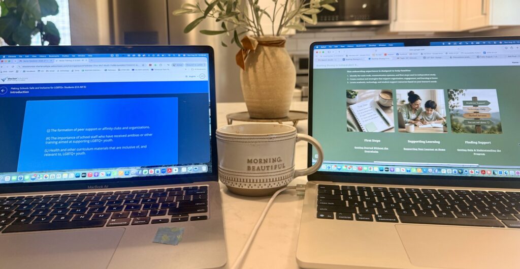 Two laptops on a kitchen island. One displays an online compliance training module, while the other shows an onboarding website created for new families in an independent study program. A coffee mug sits between the computers.
